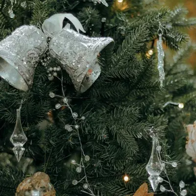 Silver bells and glass ornaments hanging on a Christmas tree.