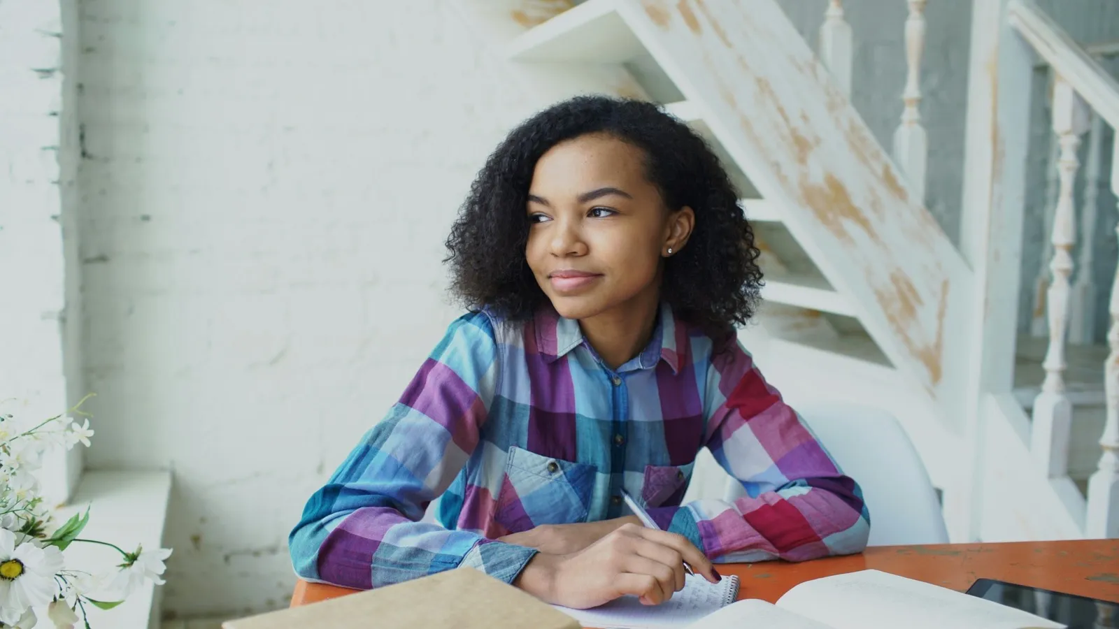 Student writing in a notebook at a desk with books