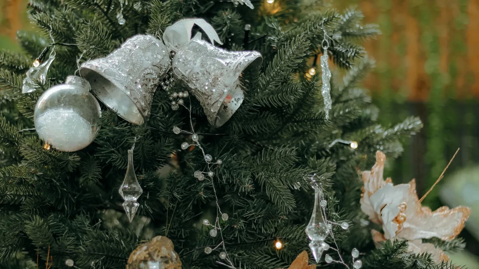 Silver bells and glass ornaments hanging on a Christmas tree.