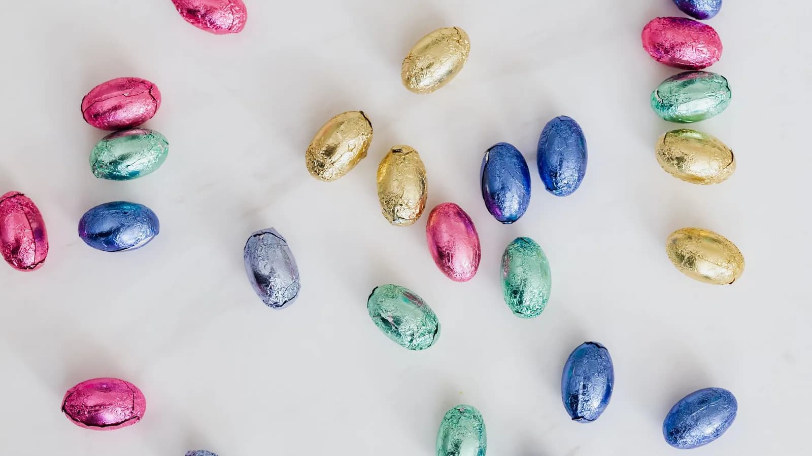 Colourful foil-wrapped chocolate Easter eggs on a white surface.