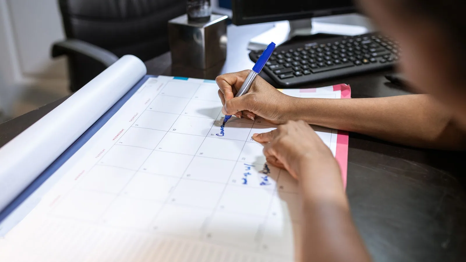 A hand writing notes on a desk planner.