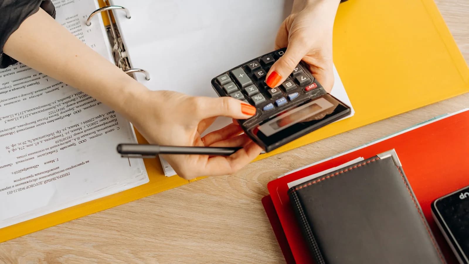 A calculator, paperwork and a yellow folder on a desk.