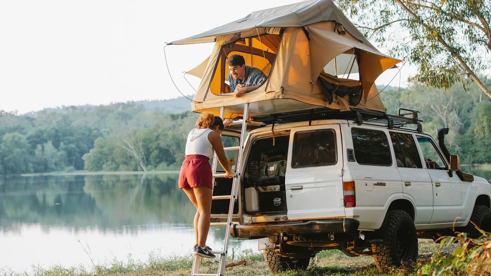 A camper with a rooftop tent parked beside a lake.