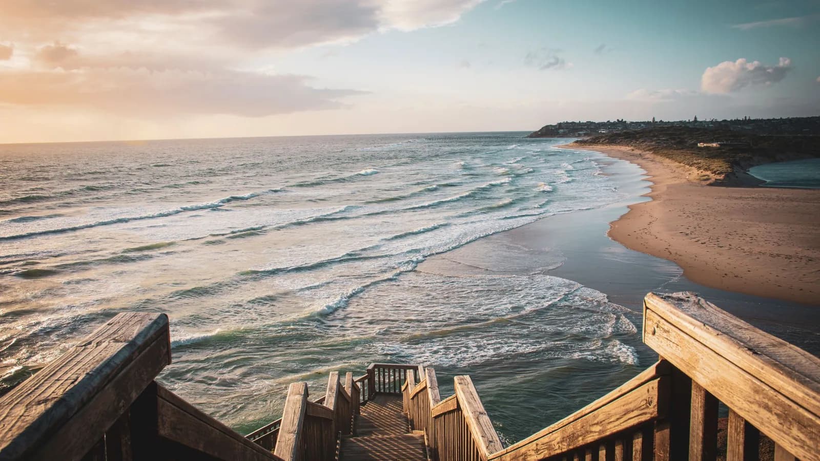 Wooden stairs leading down to a sandy beach and rolling waves.