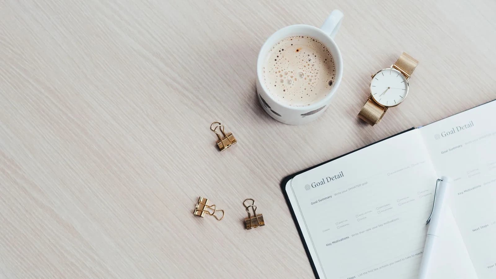 An open weekly planner beside a watch and a cup of coffee.
