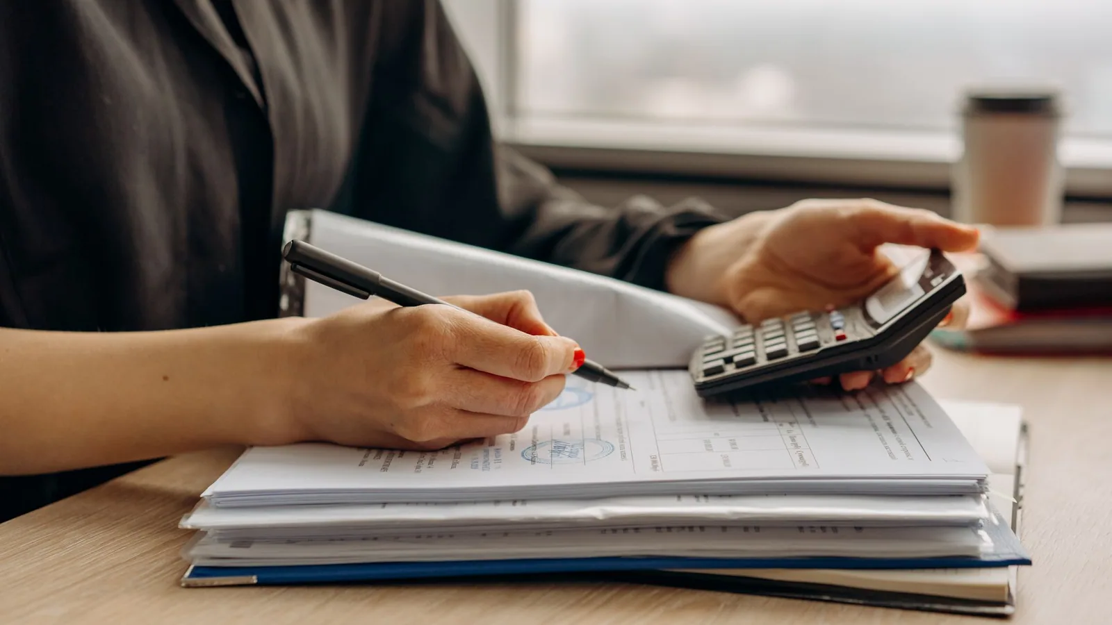 A person checking paperwork with a calculator at a desk.