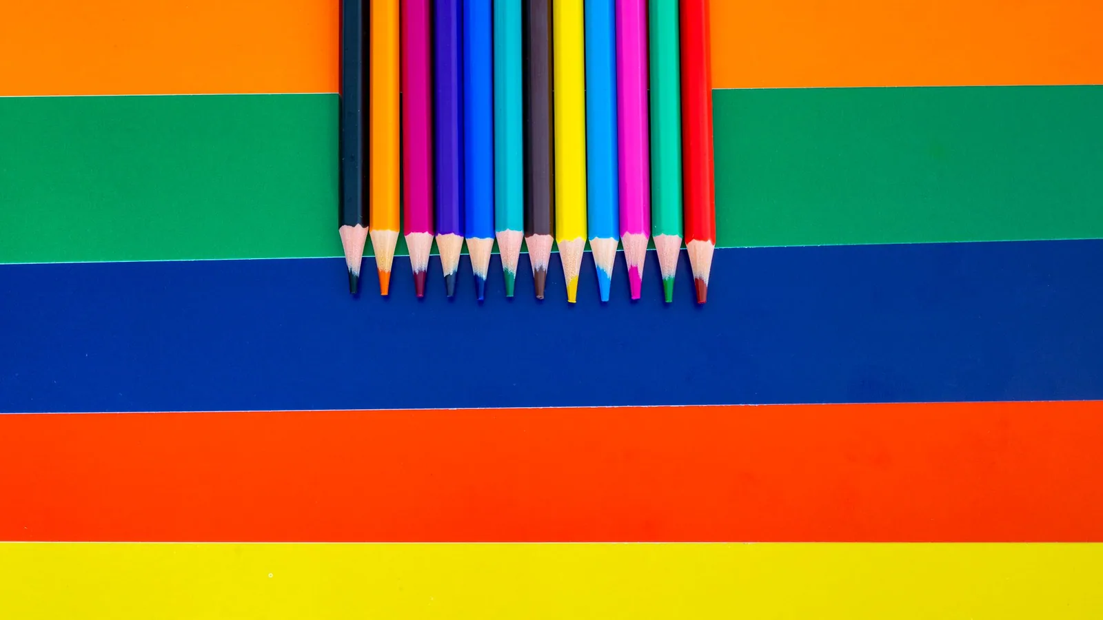 Coloured pencils arranged over bright sheets of paper.