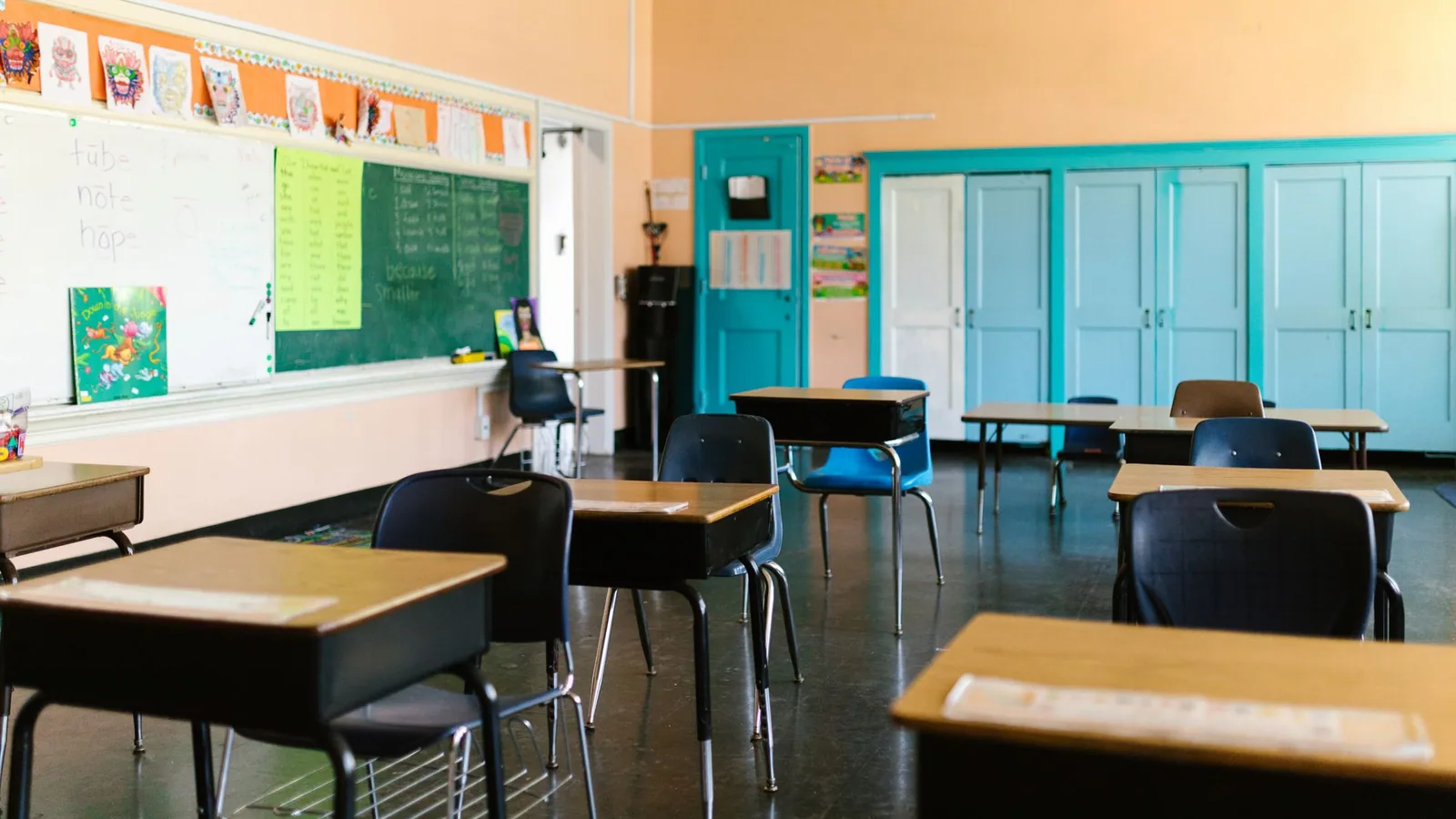 An empty classroom with blue cupboards and grouped desks.