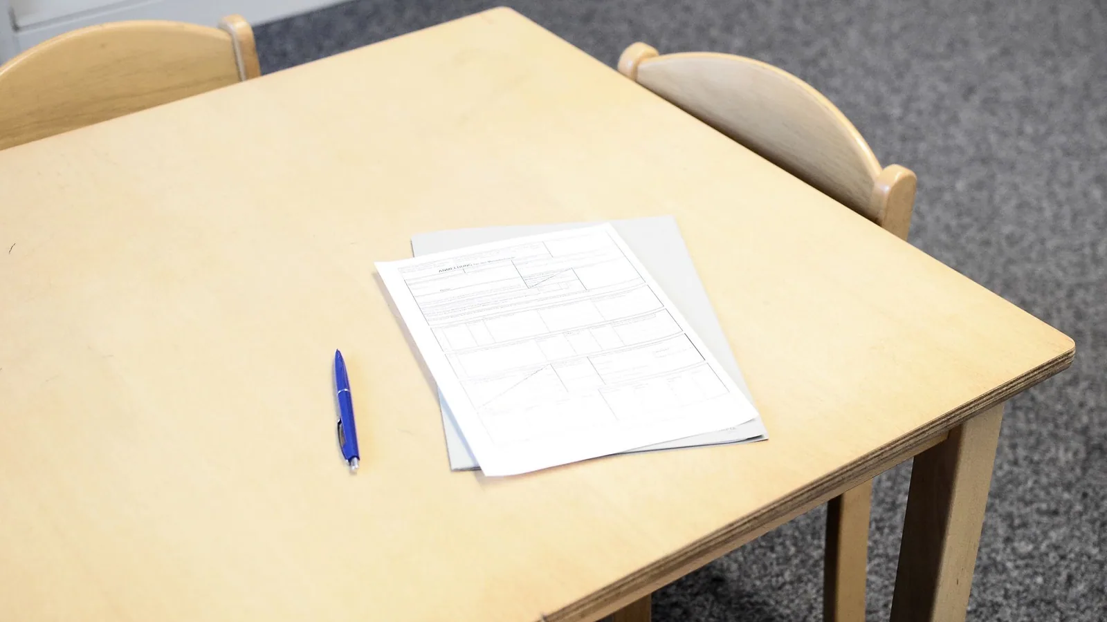 Papers and a blue pen on a wooden classroom table.