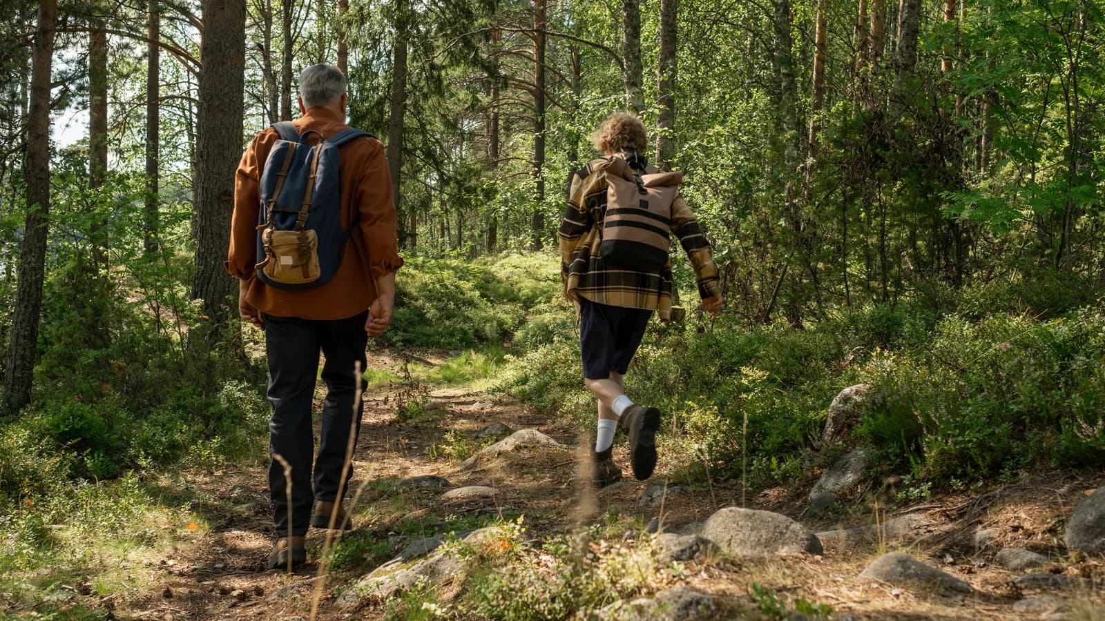 A grandfather and grandson walking along a woodland trail.