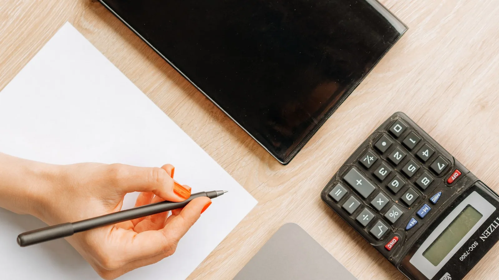 An overhead view of a hand using a calculator beside a laptop.