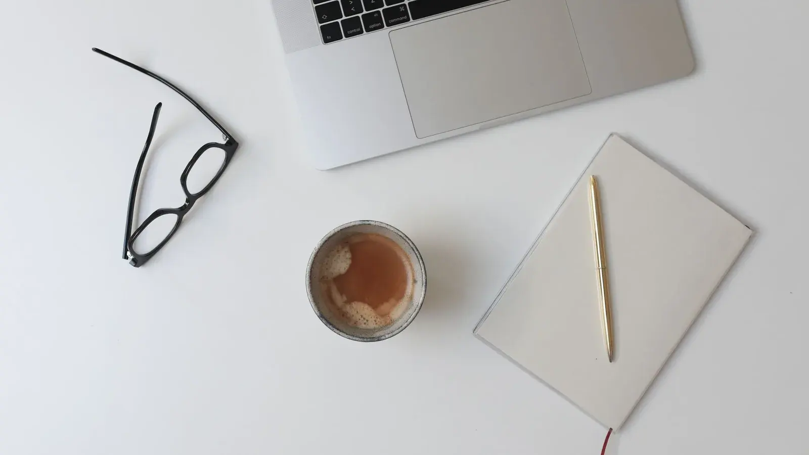 A notebook, laptop and coffee arranged on a white desk.